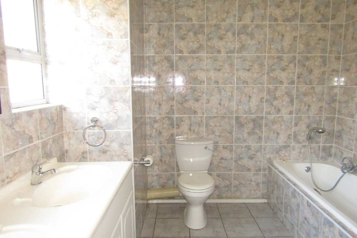 A dated bathroom featuring full-height marble-effect wall tiling, a built-in bathtub with shower attachment, a vanity basin, and a standard toilet.