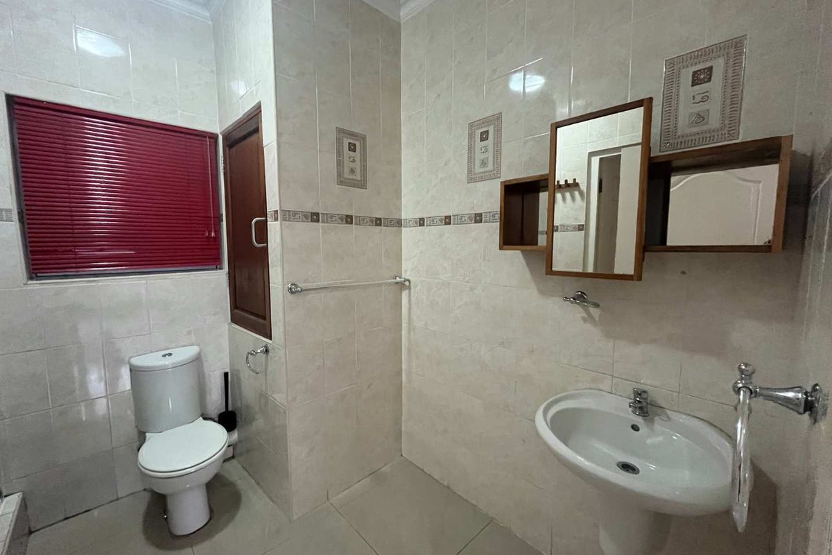 A functional bathroom featuring a pedestal basin, wall-mounted mirror cabinet, and a standard toilet with tiled walls and flooring.
