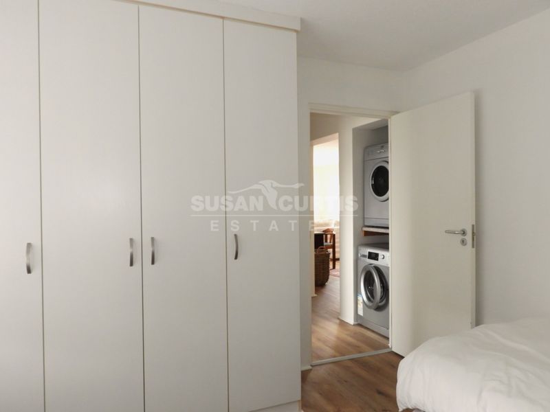 Bedroom featuring built-in wardrobes and laminate flooring, with an adjacent laundry cupboard containing stacked washer and dryer units.