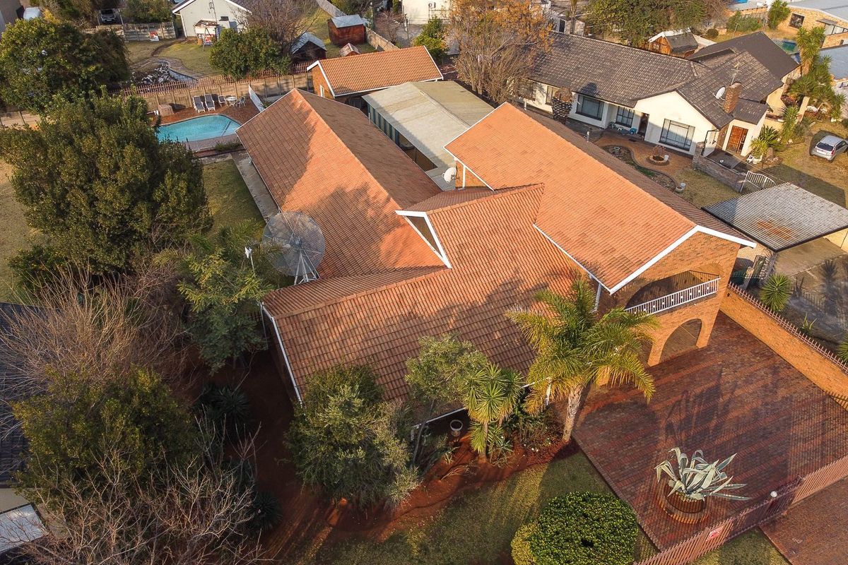 Aerial view of the property showcasing the tiled roof structure, brick paved driveway, swimming pool, and surrounding garden area.
