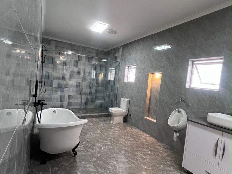 Modern bathroom featuring grey marble-look tiling, a freestanding bathtub, glass shower enclosure, wall-mounted toilet, urinal, and a sleek vanity with a vessel sink.