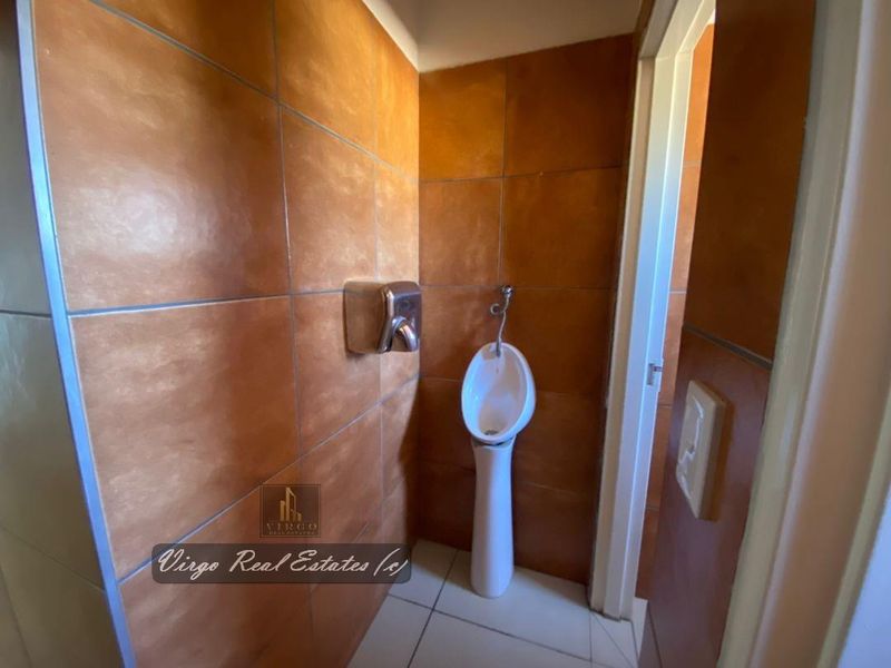 A functional hotel bathroom facility featuring a pedestal urinal and tiled wall finishes.