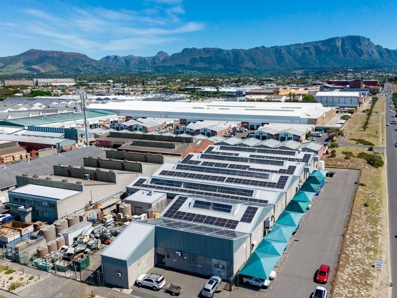 Aerial view of an industrial property featuring extensive solar panel installations on the roof, paved parking, and shade cloth structures.