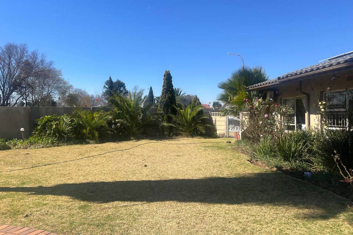 A spacious rear garden featuring a well-maintained lawn, perimeter boundary walls, and a view of the house exterior with tiled roofing and security features.