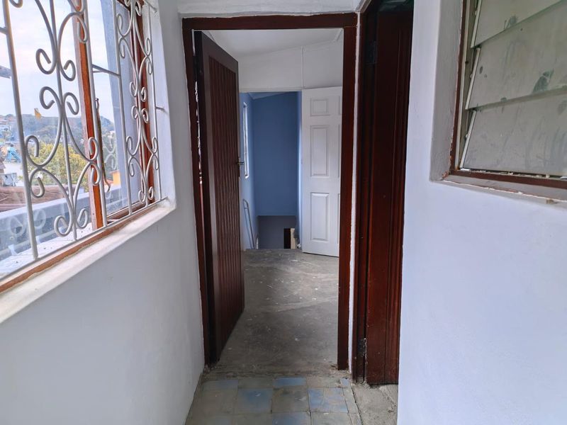 A narrow hallway featuring timber door frames, panel doors, and louver windows, leading to an interior staircase area with unfinished flooring.