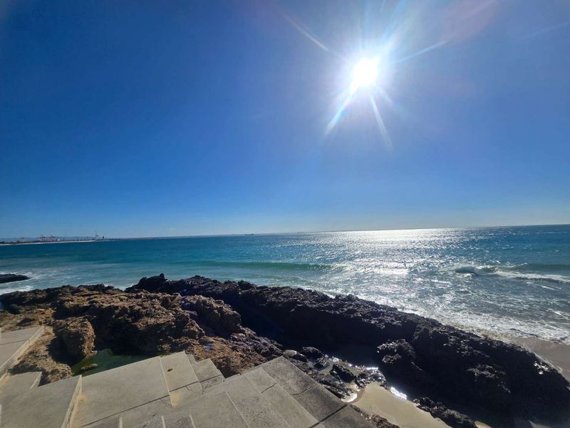 A scenic coastal view featuring concrete stairs leading down to a rocky shoreline and the ocean.