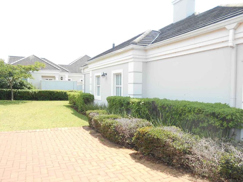A well-maintained rear exterior view of the townhouse featuring a brick paved patio area and a neat, landscaped garden with established hedging.