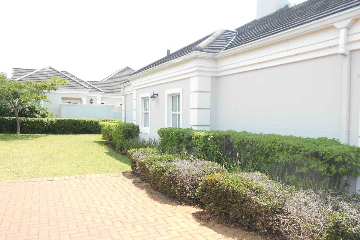 A well-maintained rear exterior view of the townhouse featuring a brick paved patio area and a neat, landscaped garden with established hedging.