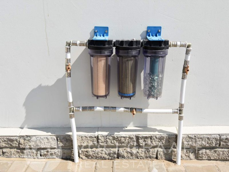 A wall-mounted triple stage water filtration system installed on the exterior of the property.