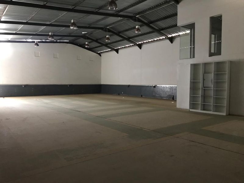 Spacious industrial warehouse unit featuring high ceilings with exposed steel trusses, concrete flooring, built-in shelving, and an internal mezzanine window.