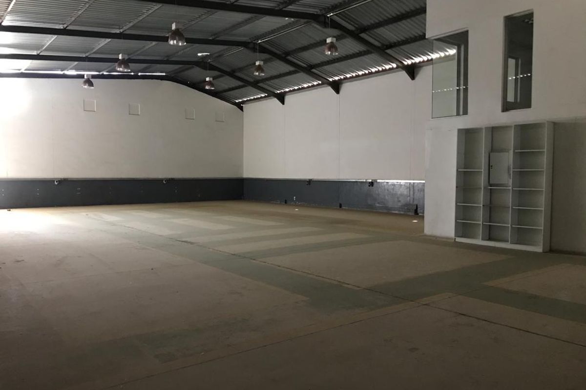 Spacious industrial warehouse unit featuring high ceilings with exposed steel trusses, concrete flooring, built-in shelving, and an internal mezzanine window.