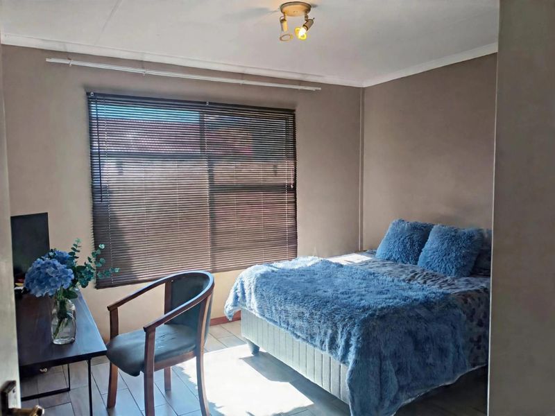 A functional bedroom featuring tiled flooring, neutral wall tones, and venetian blinds, providing a comfortable and well-lit sleeping space.