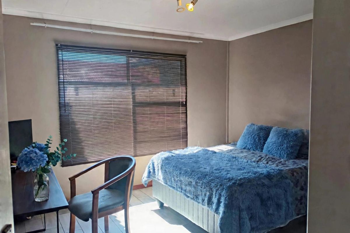 A functional bedroom featuring tiled flooring, neutral wall tones, and venetian blinds, providing a comfortable and well-lit sleeping space.
