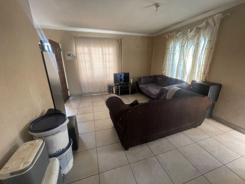 A living room featuring tiled flooring and standard cornicing, requiring cosmetic updates to the wall finishes to improve the overall aesthetic.