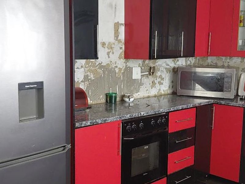 Kitchen featuring red and black cabinetry, dark tiled flooring, and a built-in oven, currently requiring wall surface repairs and backsplash installation.