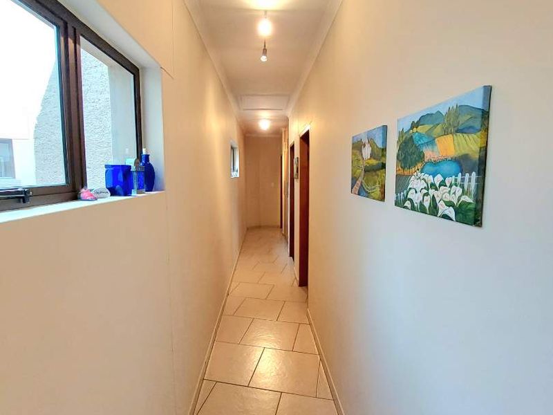 A clean, well-lit hallway featuring neutral tiled flooring and modern aluminium window frames, providing access to multiple rooms.