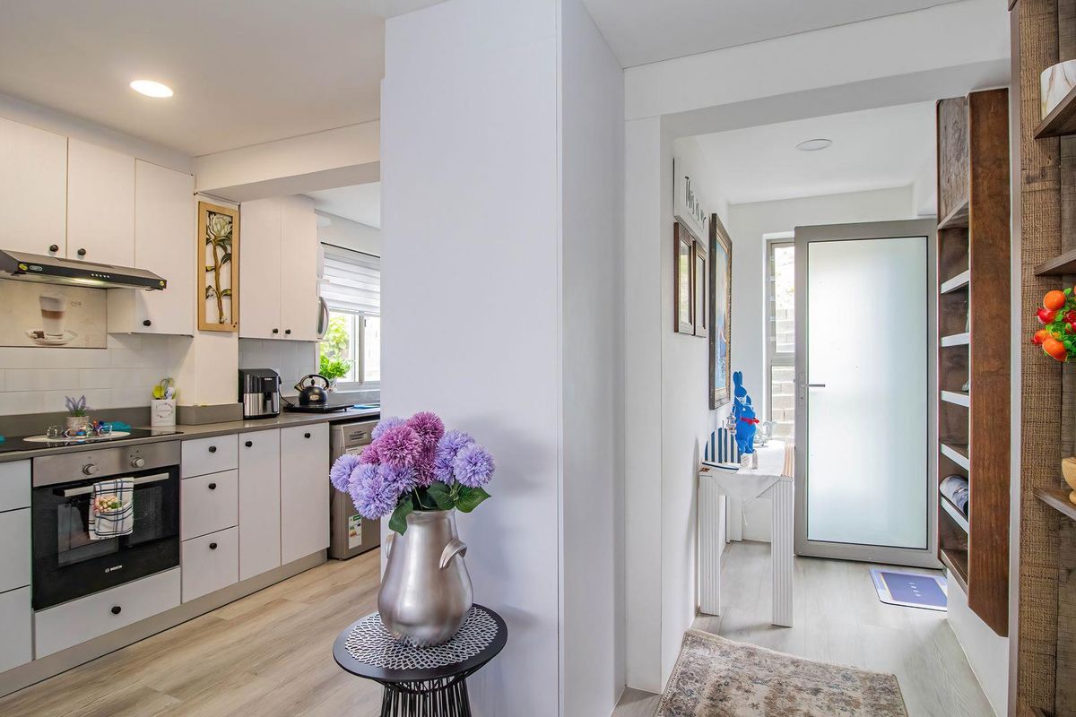 A bright, modern kitchen featuring white cabinetry, subway tile backsplash, integrated appliances, and light wood-look flooring, leading to a separate entrance area.