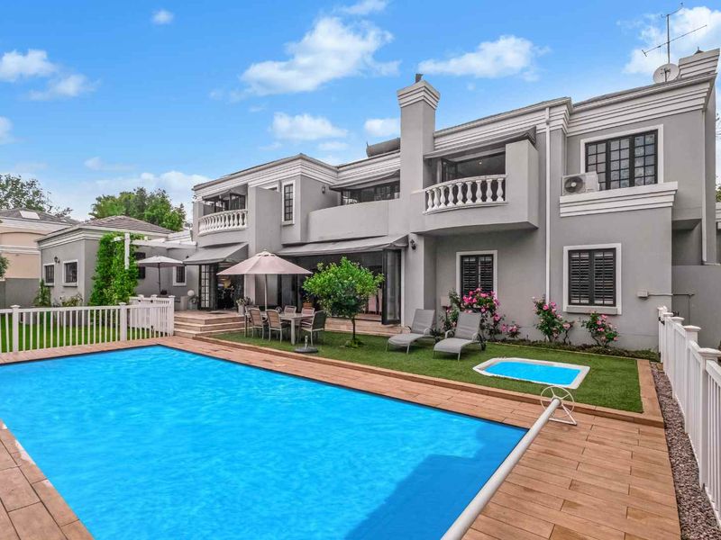 Rear view of a two-story house featuring a swimming pool, timber decking, a manicured lawn, and a balcony.