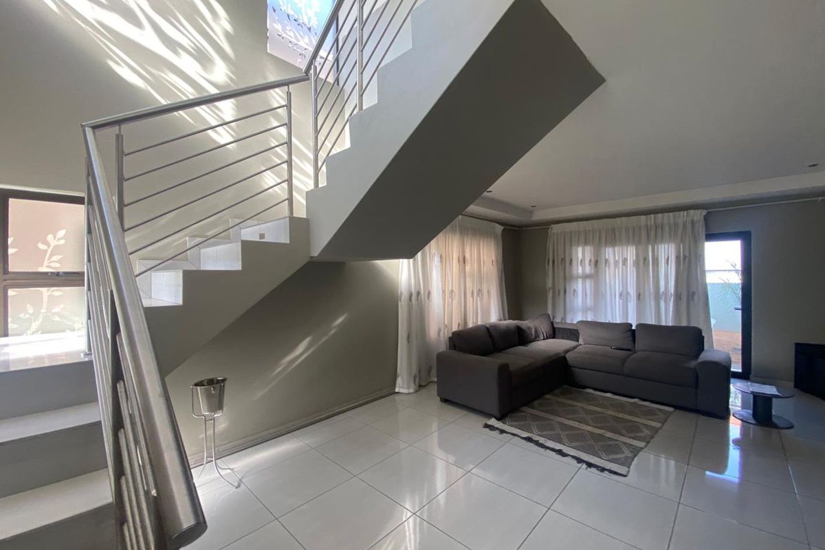 Spacious living area featuring modern tiled flooring, a prominent staircase with stainless steel balustrades, and direct access to the outdoor area via sliding doors.