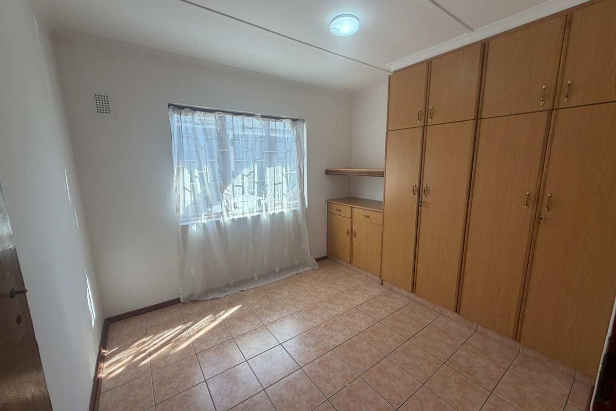 A clean, empty bedroom featuring tiled flooring and extensive built-in wooden cabinetry for storage.