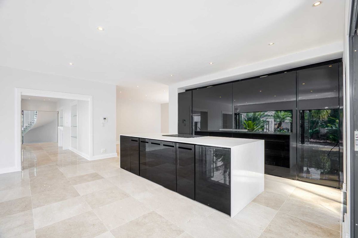 Modern open-plan kitchen featuring high-gloss black cabinetry, a central island with a built-in cooktop, and light-toned stone floor tiles.