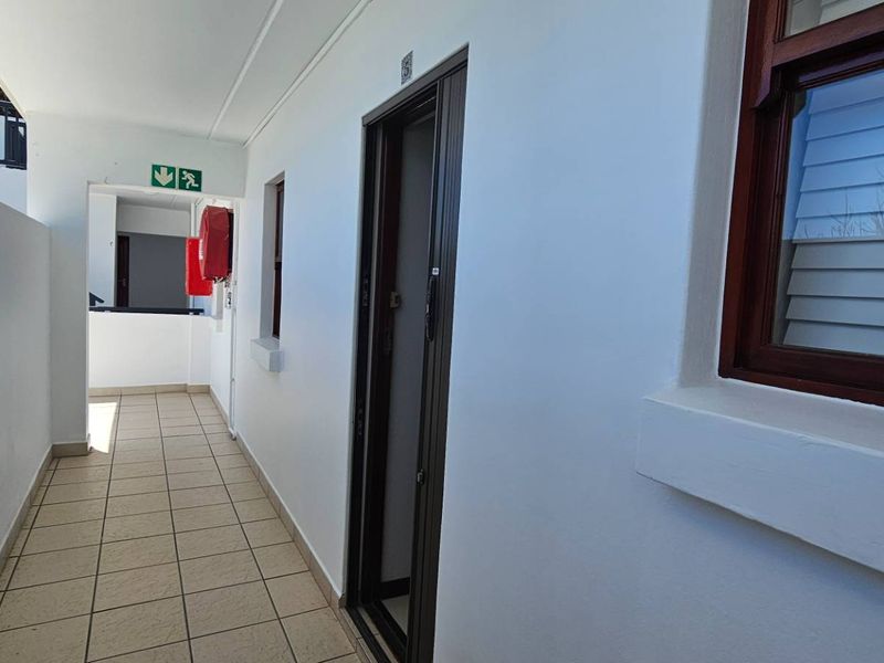 A clean, well-maintained apartment hallway featuring tiled flooring, emergency safety equipment, and access to the unit entrance.