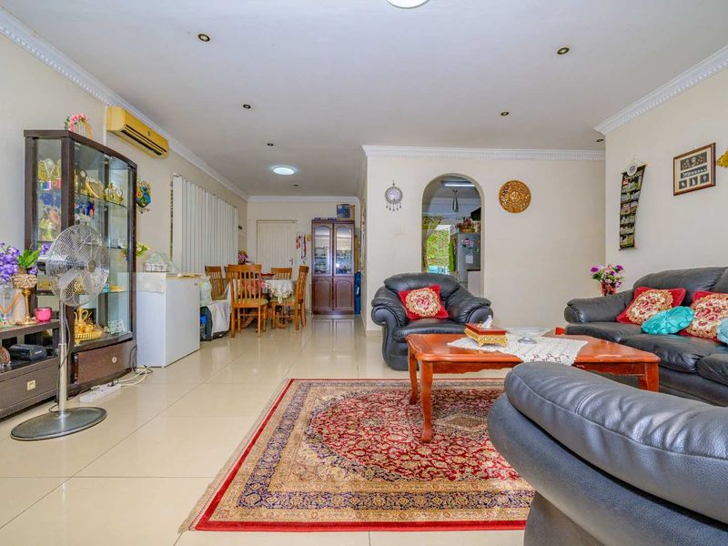 Spacious open-plan living and dining area featuring tiled flooring, recessed lighting, and a wall-mounted air conditioning unit, leading through an archway to the kitchen.