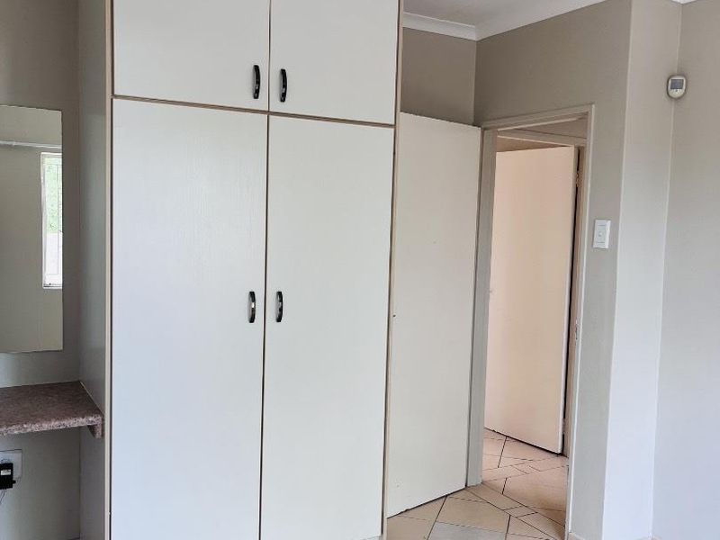 A clean, empty bedroom featuring built-in white cupboards, tiled flooring, and a small vanity area with a mirror.