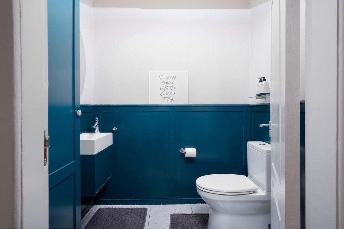 A modern powder room featuring bold blue wainscoting, a wall-mounted vanity with basin, and a clean white toilet.