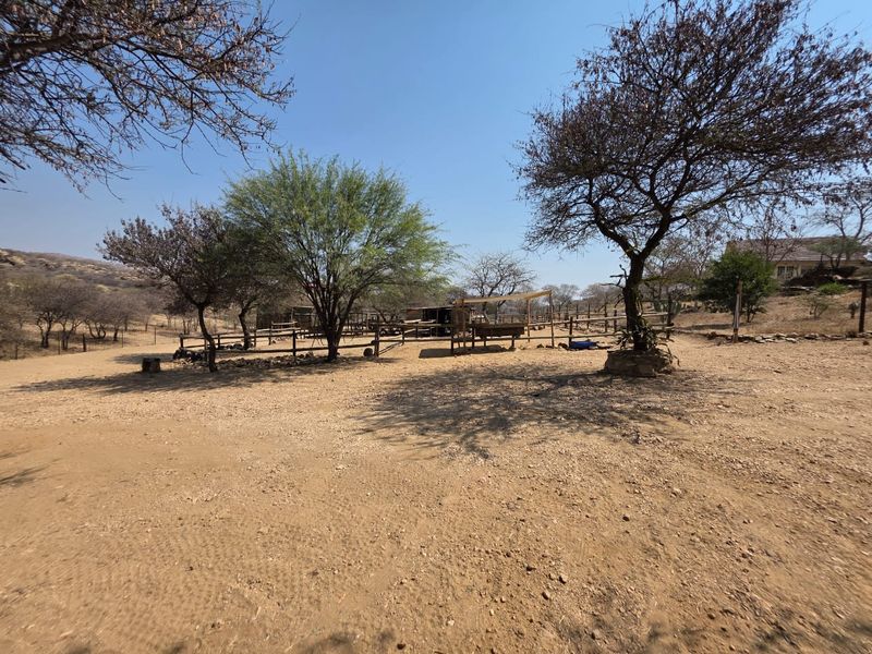 A spacious outdoor area featuring mature trees, gravel ground cover, and wooden post and rail fencing, suitable for various rural or lifestyle uses.