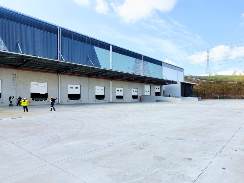 Industrial warehouse exterior featuring multiple loading docks with dock levelers, a large concrete hardstand area, and modern metal cladding.