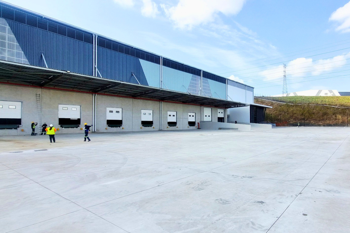 Industrial warehouse exterior featuring multiple loading docks with dock levelers, a large concrete hardstand area, and modern metal cladding.
