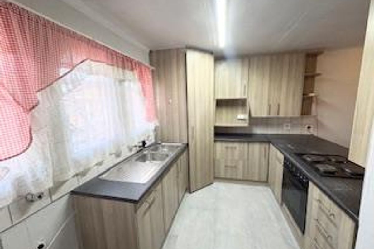 A functional kitchen featuring light wood-look cabinetry, dark laminate countertops, a built-in oven, hob, and a double bowl stainless steel sink.