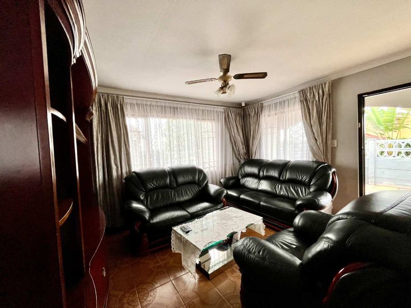 A comfortable living room featuring tiled flooring, a ceiling fan, and large windows with security bars, offering a functional and well-lit space.