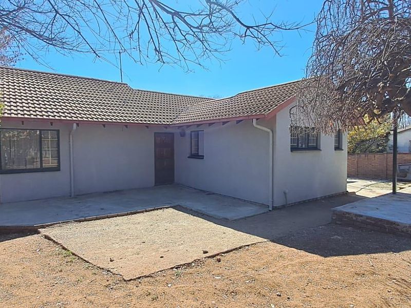 Rear view of the house featuring a tiled roof, concrete patio area, and brick boundary wall in a spacious backyard setting.