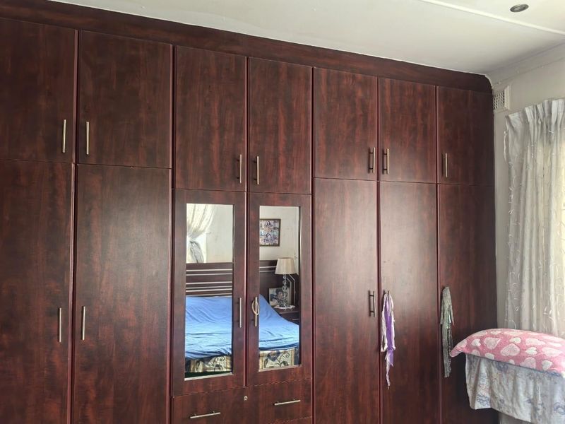 A bedroom featuring extensive dark wood-finish built-in cupboards with integrated mirrored panels, providing ample storage space.