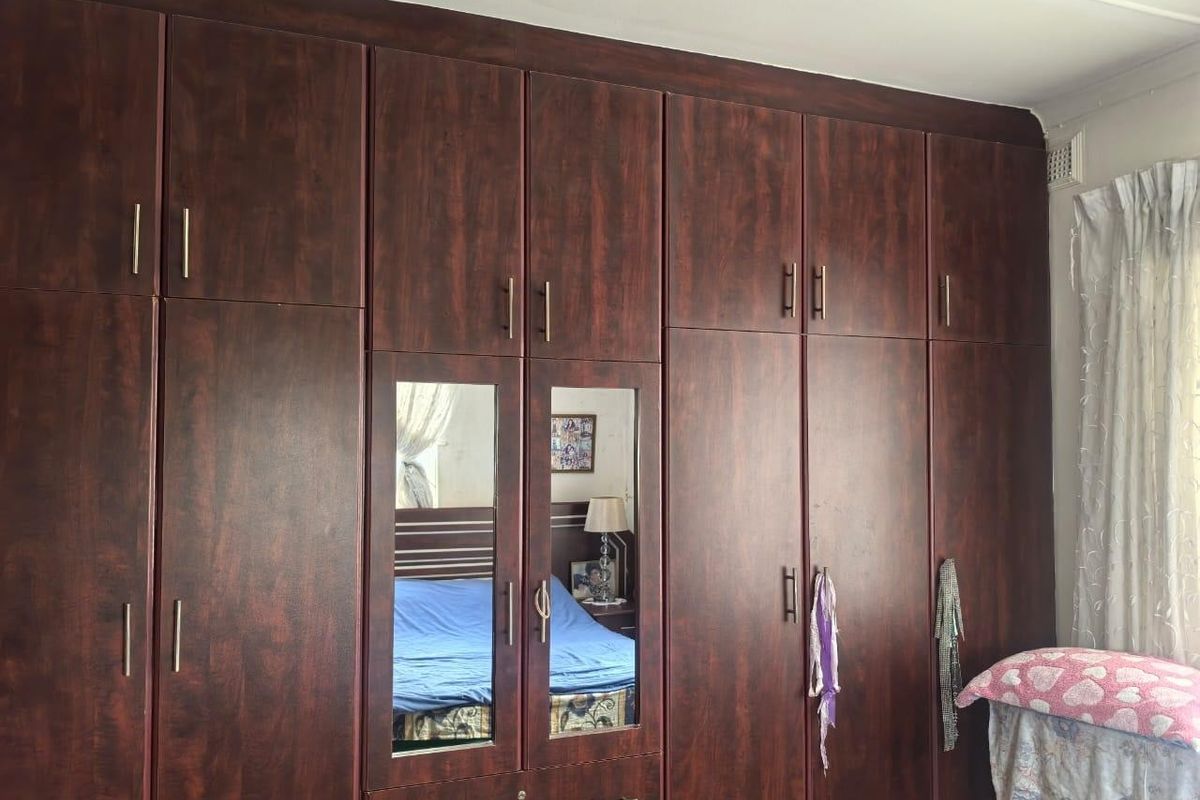 A bedroom featuring extensive dark wood-finish built-in cupboards with integrated mirrored panels, providing ample storage space.