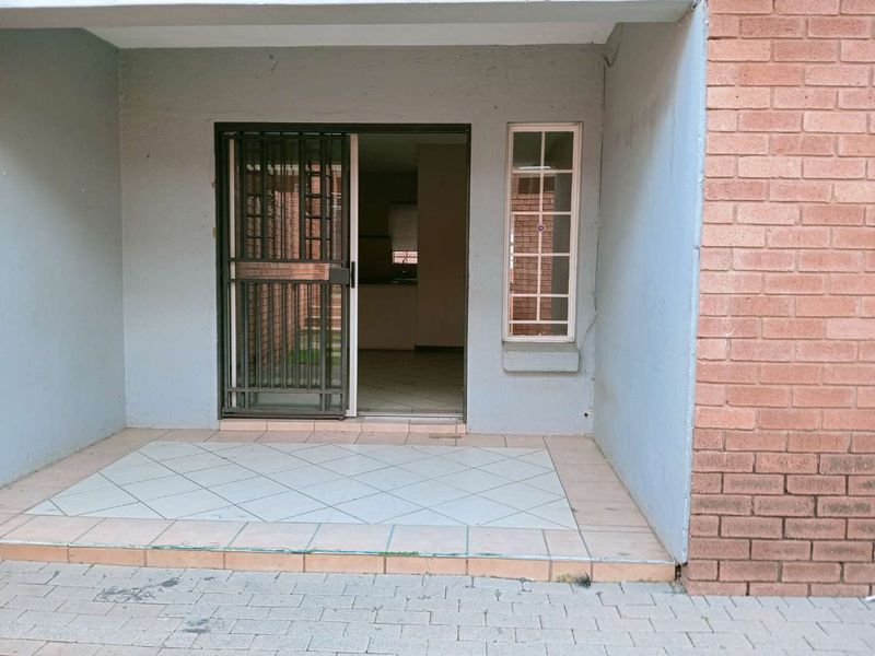 A covered patio area featuring tiled flooring, a security gate, and access to the interior, showing signs of wear on the exterior finishes.