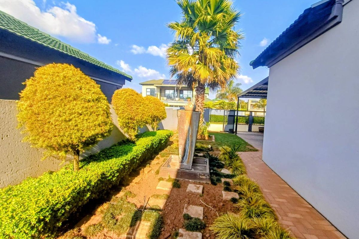 A well-maintained rear garden area featuring a central water feature, paved walkway, and established landscaping between the property structures.