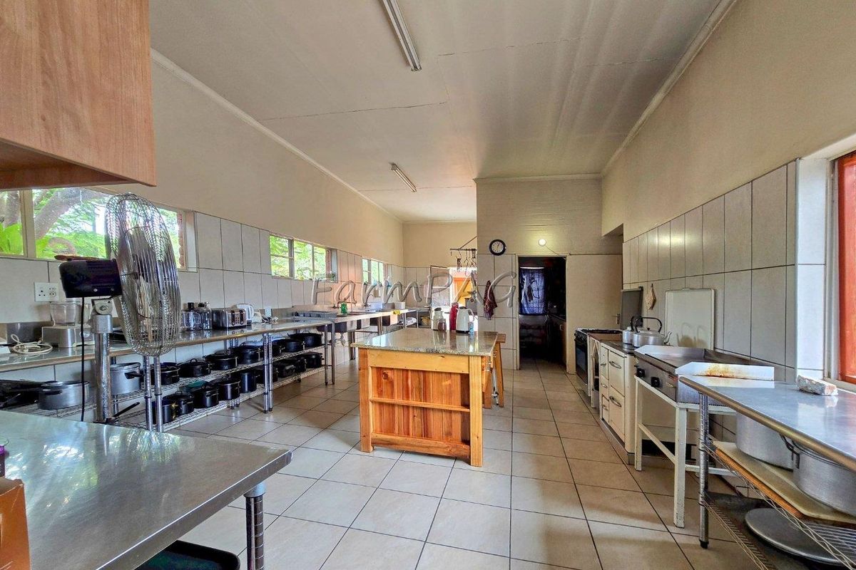 A spacious commercial-style kitchen featuring stainless steel work surfaces, tiled walls, and a central wooden island, suitable for high-volume food preparation.