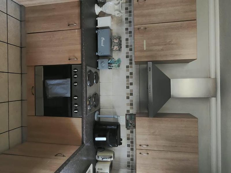 A functional kitchen featuring wood-look cabinetry, dark laminate countertops, a built-in oven, electric hob, and a stainless steel extractor fan.