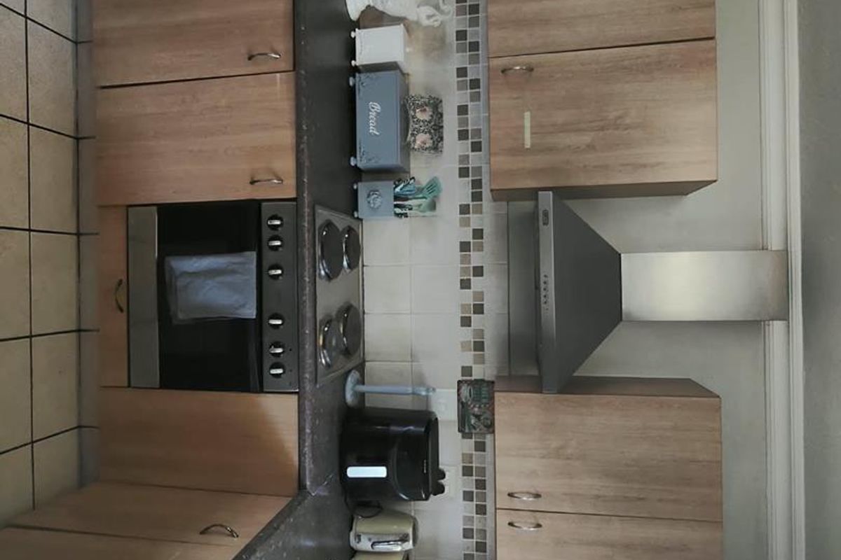 A functional kitchen featuring wood-look cabinetry, dark laminate countertops, a built-in oven, electric hob, and a stainless steel extractor fan.