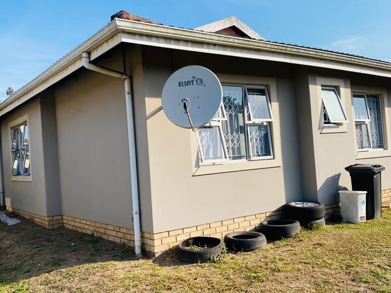 Rear exterior view of the townhouse featuring painted walls, aluminium window frames with security bars, and a satellite dish installation.