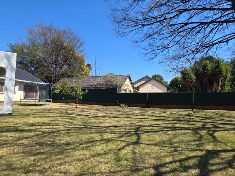 A spacious, well-maintained rear garden featuring a large lawn area, perimeter fencing, and mature trees providing shade.