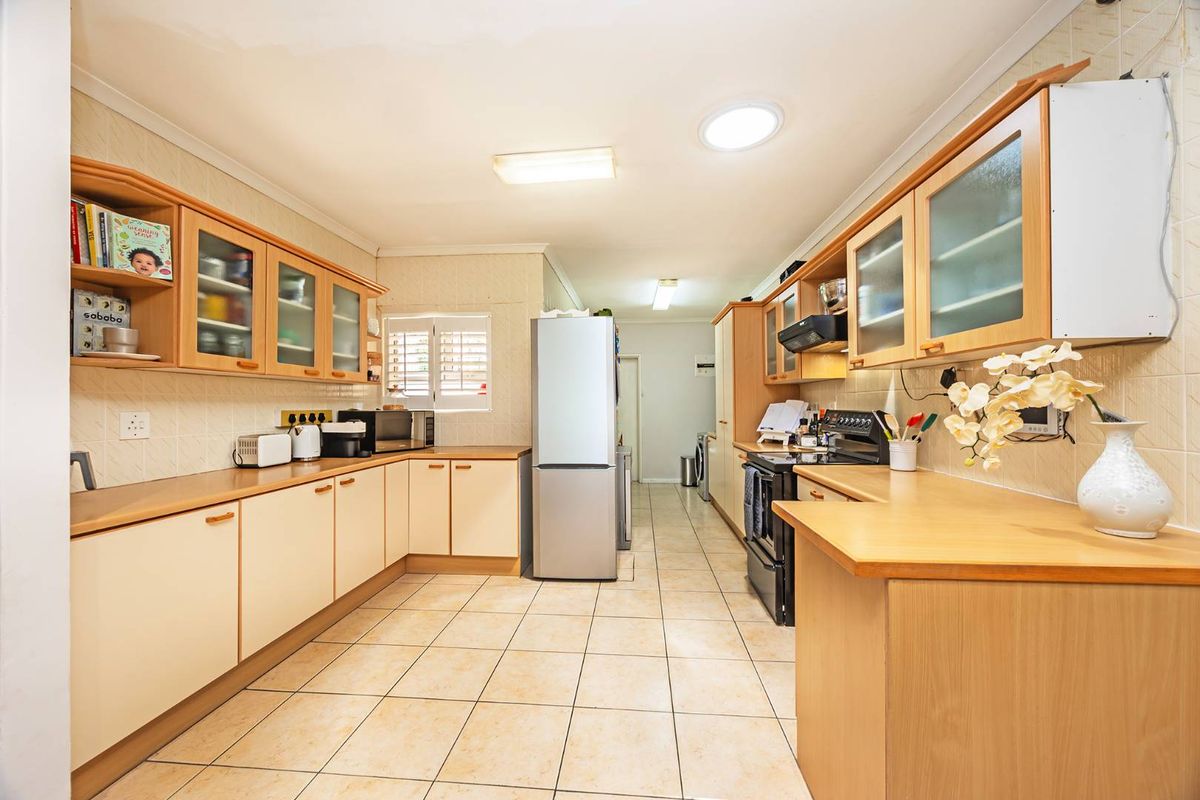 A functional galley-style kitchen featuring light wood cabinetry, tiled flooring, and built-in cooking appliances, offering ample counter space and storage.