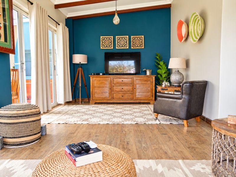 A well-maintained living room featuring warm laminate flooring, exposed ceiling beams, and a striking blue accent wall with direct access to the patio.