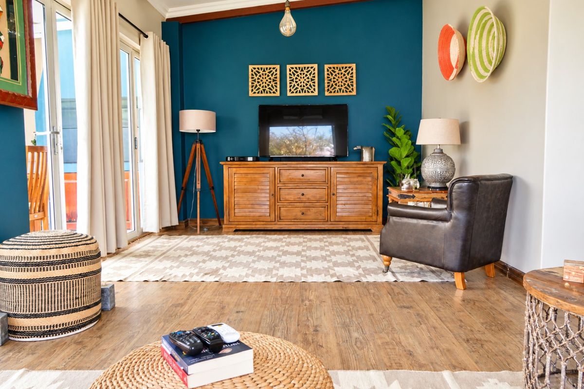 A well-maintained living room featuring warm laminate flooring, exposed ceiling beams, and a striking blue accent wall with direct access to the patio.