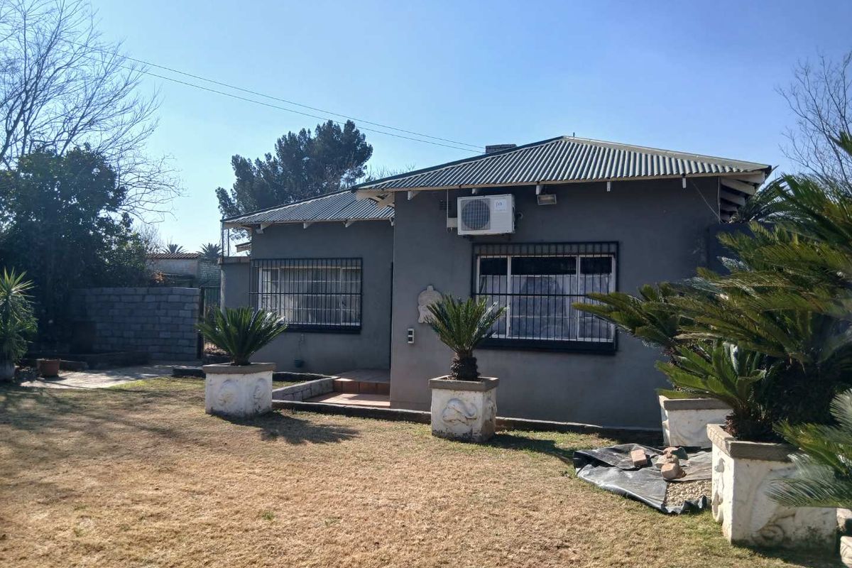 Rear view of a single-story house featuring a corrugated metal roof, security bars on windows, and an installed air conditioning unit.