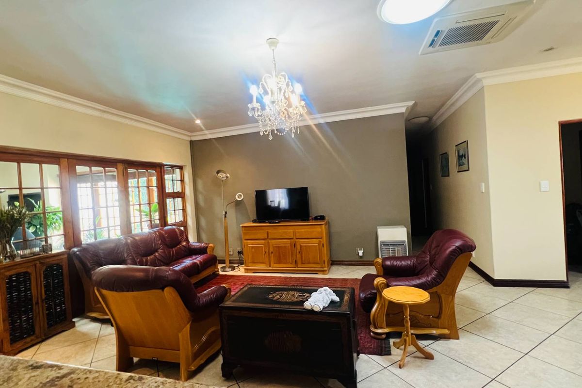 Spacious living room featuring tiled flooring, crown molding, and a central chandelier, with large wooden-framed glass doors leading to an adjacent area.