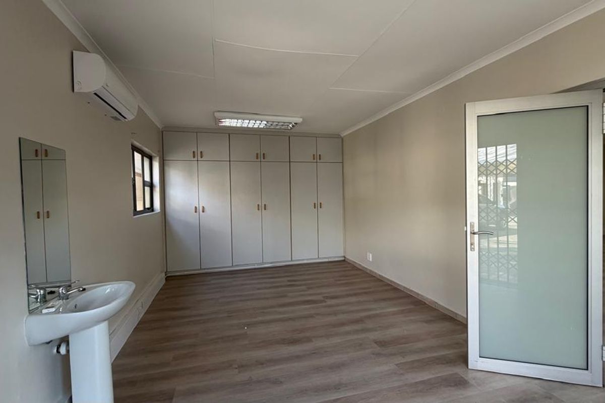 A clean, empty office space featuring laminate flooring, built-in storage cabinetry, a private pedestal sink, and a wall-mounted air conditioning unit.